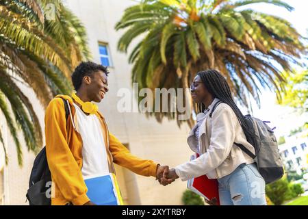 Side view of two young cool african university students shaking hands outside the university Stock Photo