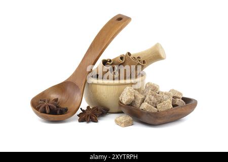 Star anise in a wooden spoon, wooden mortar filled with cinnamon sticks and brown sugar cubes in a wooden bowl isolated on white background Stock Photo