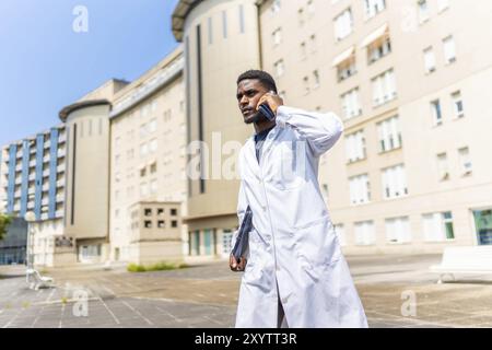 Busy african doctor talking to the mobile with serious expression walking outside the hospital Stock Photo