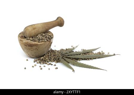 Hemp seeds in wooden rustic-style mortar near pestle and cannabis plant leaf isolated on white background Stock Photo
