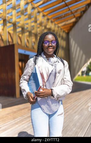 Vertical portrait of an African young woman standing outside the university smiling at camera holding folders Stock Photo