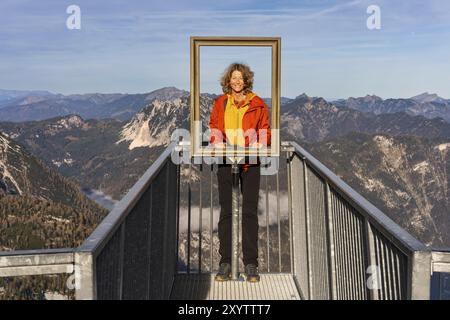 A hiker stands on the 5fingers viewpoint and looks through the picture frame. View from the Dachstein Krippenstein. Autumn, good weather. Some clouds Stock Photo