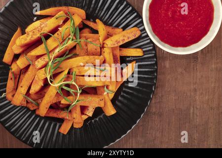 An overhead photo of roasted sweet potato fries on a plate with rosemary, a red sauce and copy space Stock Photo