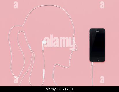 Woman head outline made by a headphone cord plugged into iPhone 5s smartphone. Music concept on pink background Stock Photo