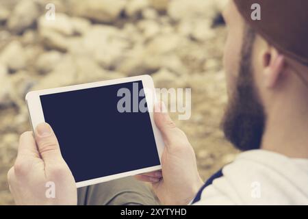 Close-up of a horde in a brown cap in the open air holds a white tablet pc in his hands. A bearded man looks at the tablet. OTS view from behind the s Stock Photo