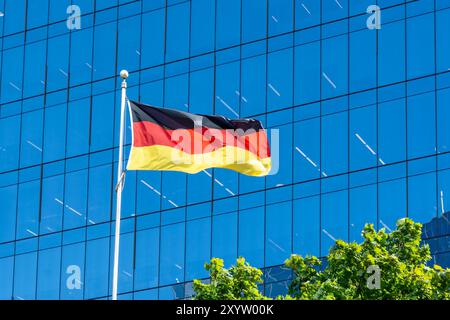 A national flag of Germany waving in the wind with a glass building in the background. Stock Photo