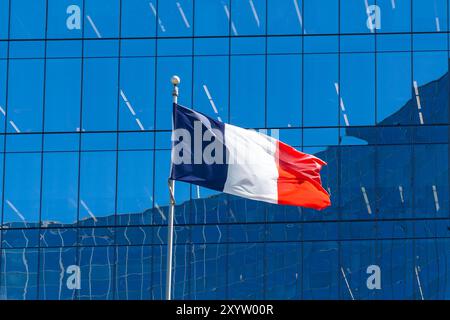 A national flag of France waving in the wind with a glass building in the background. Stock Photo