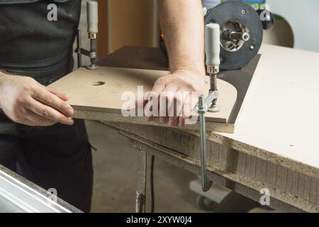 Close up Master clamps the workpiece with a dvp clamp to the workbench and on the background lies Carpentry hand router Stock Photo
