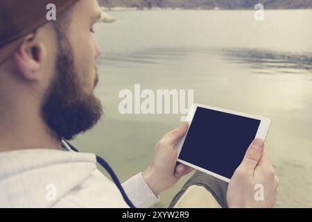 Close-up of a horde in a brown cap in the open air holds a white tablet pc in his hands. A bearded man looks at the tablet. OTS view from behind the s Stock Photo
