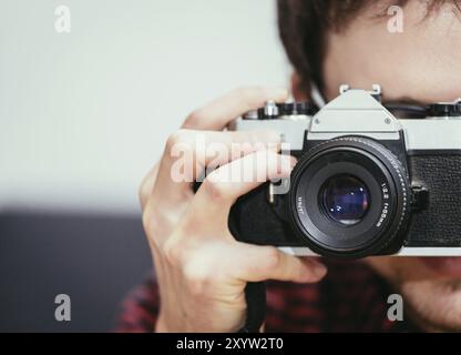 Young man in red-blue checked shirt is taking a picture with an vintage camera, retro style Stock Photo