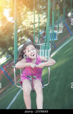 Excited little girl having fun and enjoying ride on swing carousel in park in sunny summer day Stock Photo