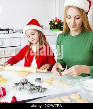 Adorable girl with her mother baking Christmas cookies in the kitchen Stock Photo
