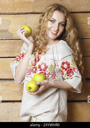 Woman in traditional dress holding apples in her hands. Wooden background Stock Photo