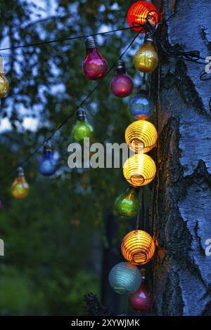 String of lights hanging on the tree. Garden party. Romantic place. Colorful light bulbs. Evening atmosphere, festive mood. Weekend, vacation or every Stock Photo