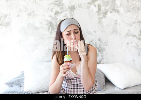 Sad lonely woman on her Birthday holding cupcake in her bedroom Stock Photo