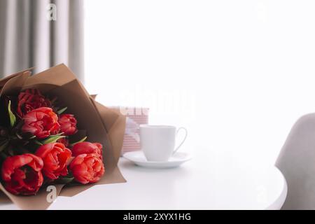 Red tulips bouquete on table, white coffee cup. Concept for greeting card for mothers day, international womans day or valentines day concept, birthda Stock Photo