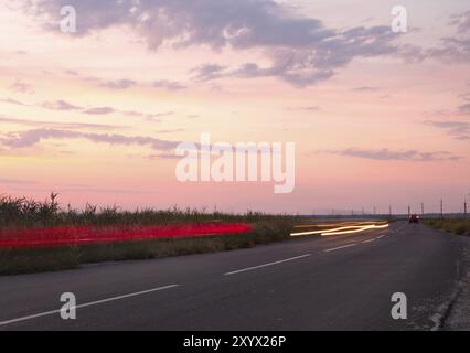 Traffic light trails on country road at sunset Stock Photo