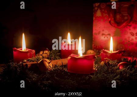 Decorated Advent wreath made of fir branches with burning red candles against a black background Stock Photo