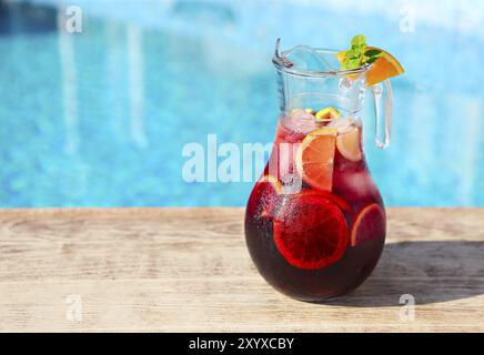 Glass jug of iced sangria with strawberry, orange, apple and lemon by the pool Stock Photo