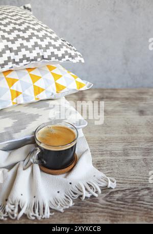 Yellow and grey pillows and cup of coffee on the wall background. Close up Stock Photo