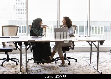 Happy multiethnic female office friends chatting at large meeting table Stock Photo