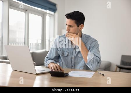 Serious freelance accountant working from home, using calculator, bank application Stock Photo