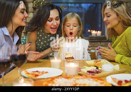 Pretty child looking at tasty birthday cake with mother and friends Stock Photo