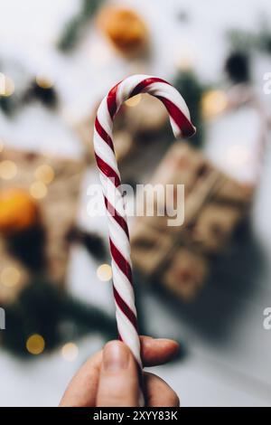 Christmas gifts, hand holds lollipop, tangerine on white wooden background. Stock Photo