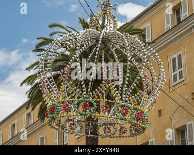 Colourful crown of pearls as decoration on a palm tree in front of a yellow building and blue sky, Ajaccio, Corsica, Mediterranean Sea, France, Europe Stock Photo