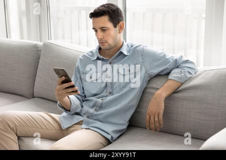 Serious relaxed young Hispanic man typing on mobile phone Stock Photo