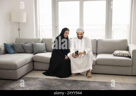 Happy Muslim Arabic couple using smartphone at home together Stock Photo