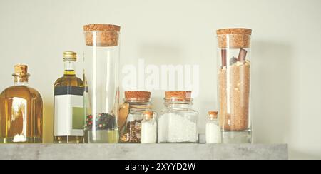 Selective focus of arranged jars with various spices and olive oil on kitchen shelf. Toned photo Stock Photo