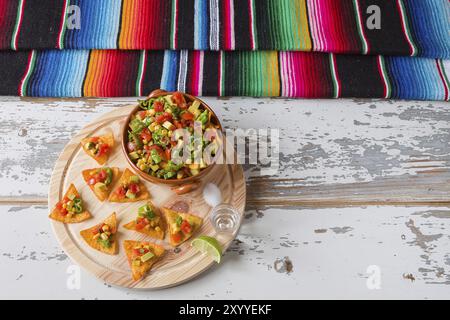 Nachos chips and vegetables in an earthenware bowl tequila lime salt and poncho seen from above Stock Photo