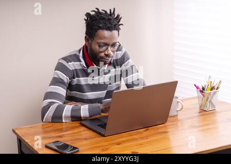 Young African American professional in casual attire working on laptop at home office. Concept of remote work, technology, and diversity in modern wor Stock Photo