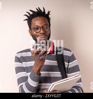 Young African American man with glasses and dreadlocks using smartphone while holding notebooks. Concept of digital learning, student life, and mobile Stock Photo