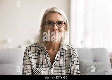 Headshot woman in glasses sit on sofa looking at camera Stock Photo