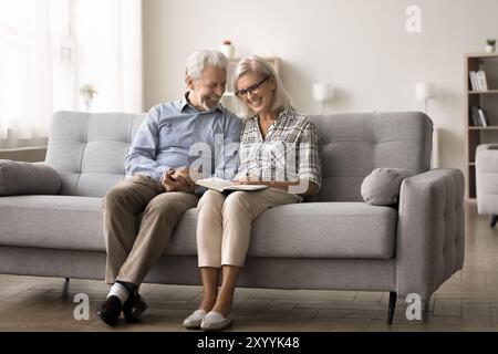 Smiling mature spouses spend peaceful pastime reading a book Stock Photo