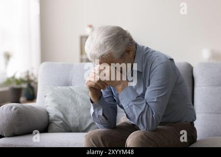 Depressed man sit on sofa, crying, covering face with hands Stock Photo