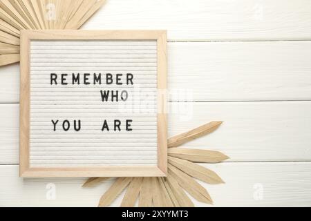 Letter board with phrase Remember Who You Are and decor elements on white wooden table, flat lay. Space for text Stock Photo