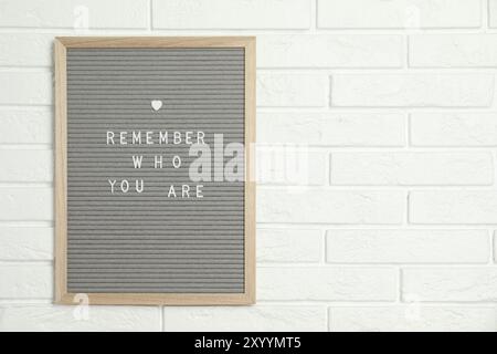 Letter board with phrase Remember Who You Are on white brick wall, space for text Stock Photo