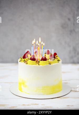 Beautiful happy birthday cake with mascarpone decorated with raspberry, pistachio and candles on the cake stand Stock Photo