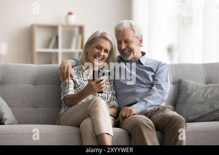 Older spouses using smartphone laughing, watching funny videos Stock Photo