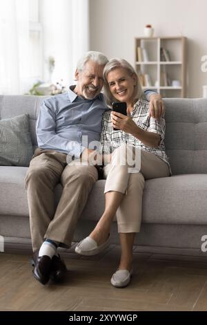 Attractive mature spouses spend pleasant time on internet using smartphone Stock Photo