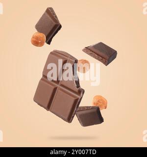 Pieces of tasty chocolate and hazelnuts falling on dark beige background Stock Photo