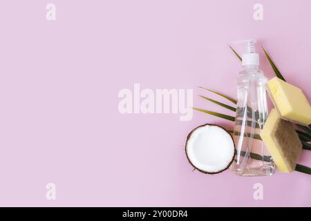 Flat lay with green palm leaf, coconut half, soap dropper, dishwashing liquid, dish soap, washcloth on pastel pink and yellow background. Stock Photo