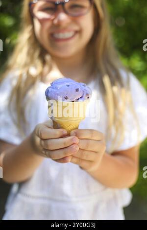 Portrait of the cute little girl with funny expression holding ice cream cone outside against bright nature background Stock Photo