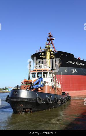 The oil tanker Unique Guaridan is towed in the harbour basin by a tugboat. Oil tanker towaged in harbour Stock Photo