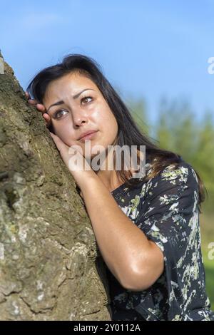 Portrait young woman leaning against tree trunk Stock Photo