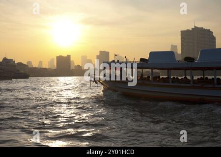 A river taxi plies the waters of the Chao Phraya river at sunrise in downtown Bangkok, Thailand, Asia Stock Photo