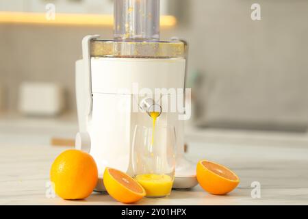 Modern juicer, oranges and glass on white marble table in kitchen Stock Photo